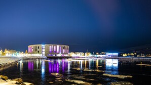 A waterfront hotel with a circular building, reflecting lights on the water, and a snow-covered shore. - Saga Apartments (Akureyri)