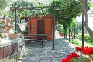 Un patio empedrado con un banco de madera y una mesa pequeña, rodeado de follaje y una pérgola.