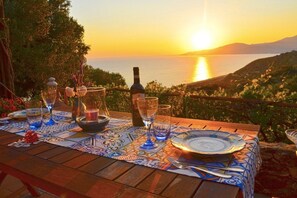 Una mesa dispuesta para una comida, con una botella y copas, frente a un atardecer sobre el agua.