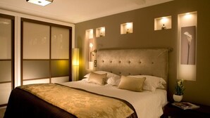 A well-lit bedroom with a large bed, a nightstand with a lamp, and a wall-mounted light fixture. - Beaufort House - Knightsbridge (London)