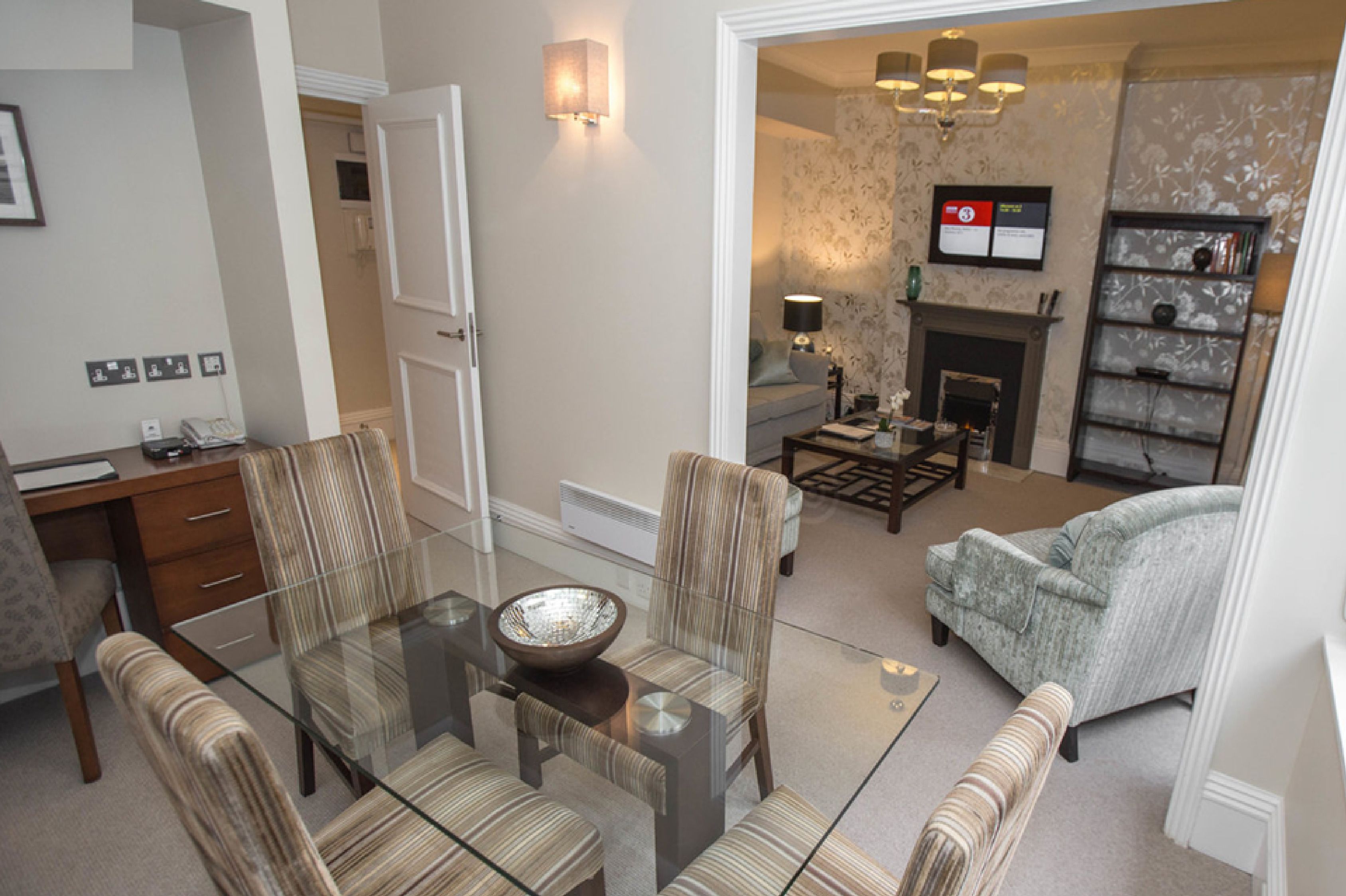 A dining area with a glass table and striped chairs, a sofa, a fireplace, and a bookshelf.