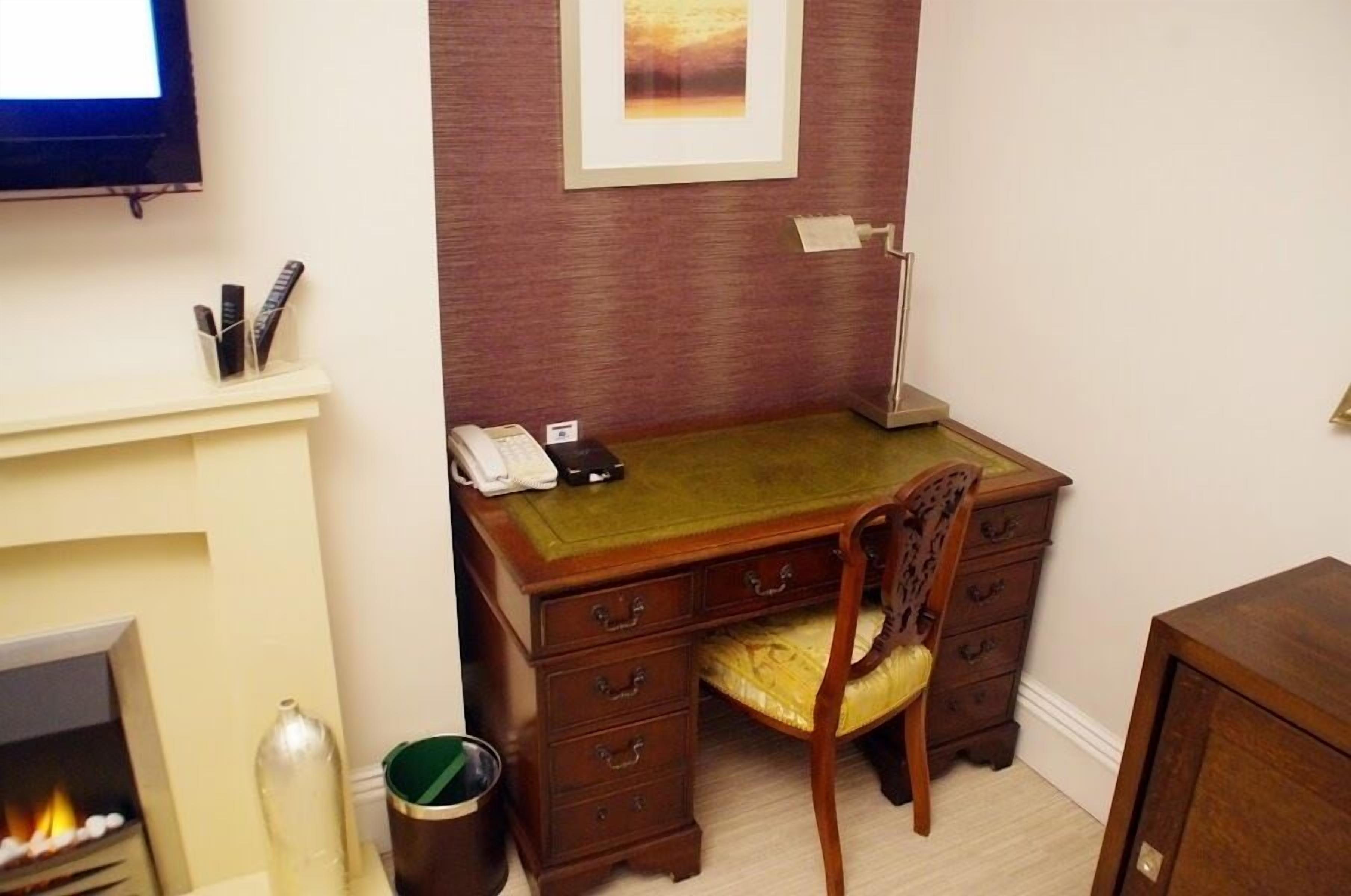 Une pièce comprenant un bureau, une chaise, une cheminée et un tableau encadré au mur.