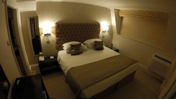 Habitación de hotel con una cama grande, dos mesitas de noche, una lámpara de pared y una ventana con cortina.