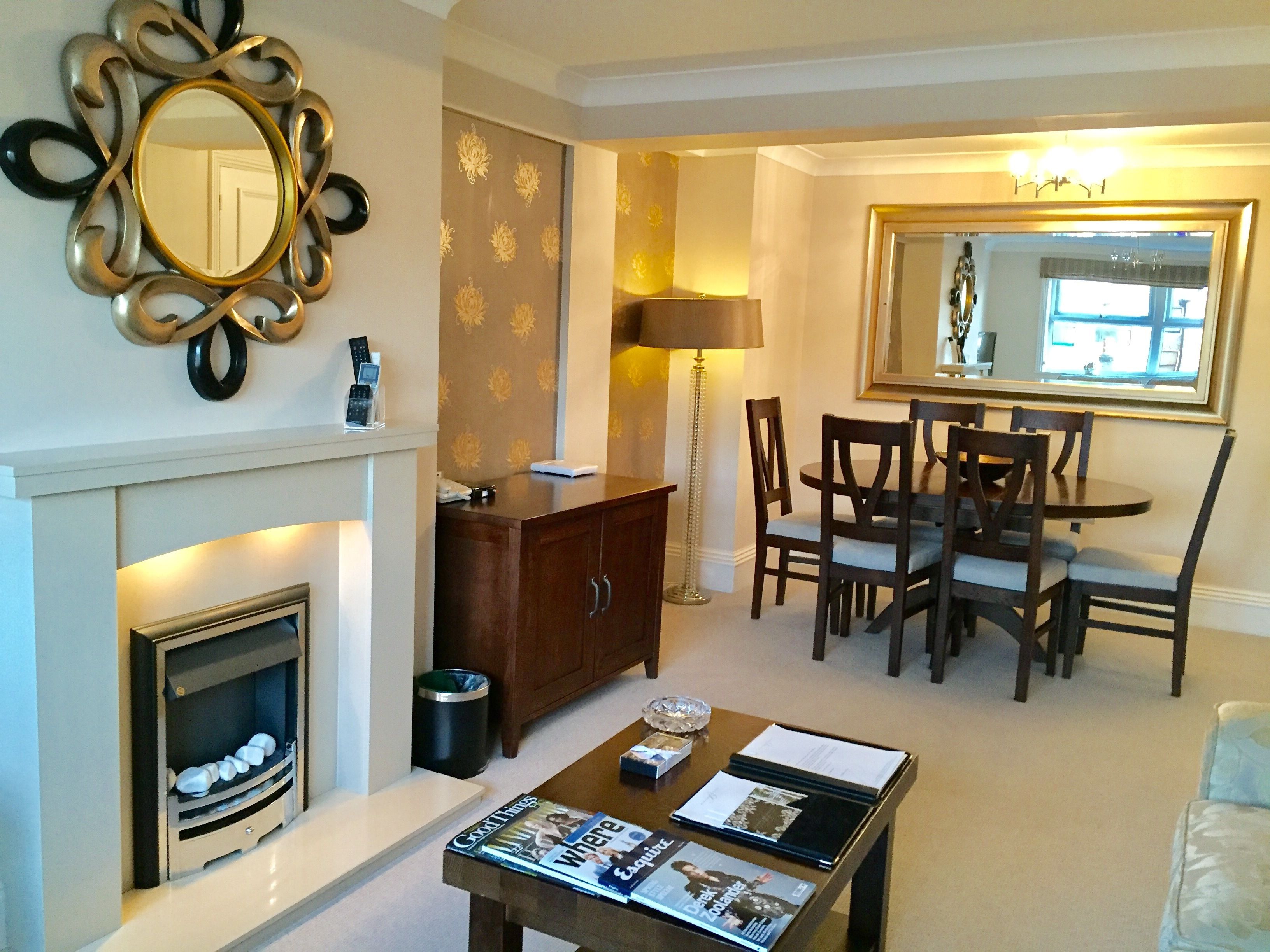 A dining area with a round table and chairs, a fireplace, a cabinet, and a mirror on the wall.
