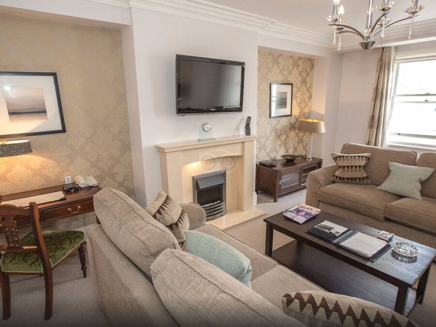 A living room with a fireplace, a television mounted on the wall, a sofa, a coffee table, and a desk with a lamp.