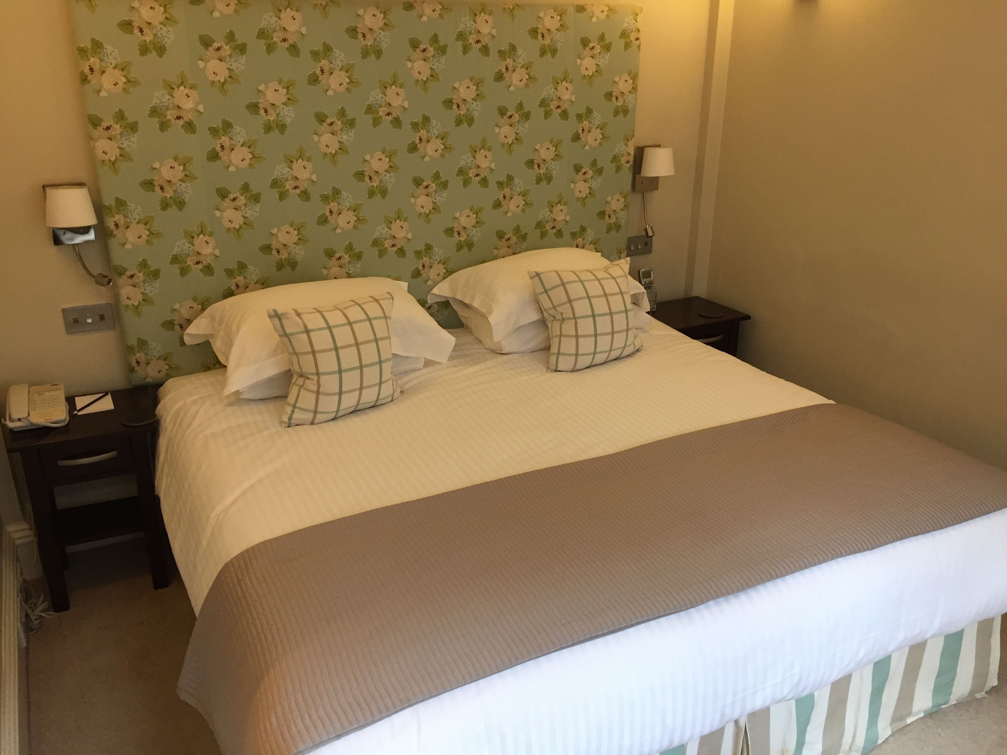 A neatly made bed with two pillows, a bedside lamp, and a floral-patterned headboard.