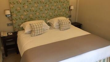 A neatly made bed with two pillows, a bedside lamp, and a floral-patterned headboard.