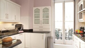 A kitchen with white cabinets, a black countertop, and a window overlooking a balcony with outdoor furniture. - Beaufort House - Knightsbridge (London)