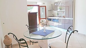 Un comedor con una mesa de vidrio, cuatro sillas, un florero con flores y vistas a una cocina y un balcón.