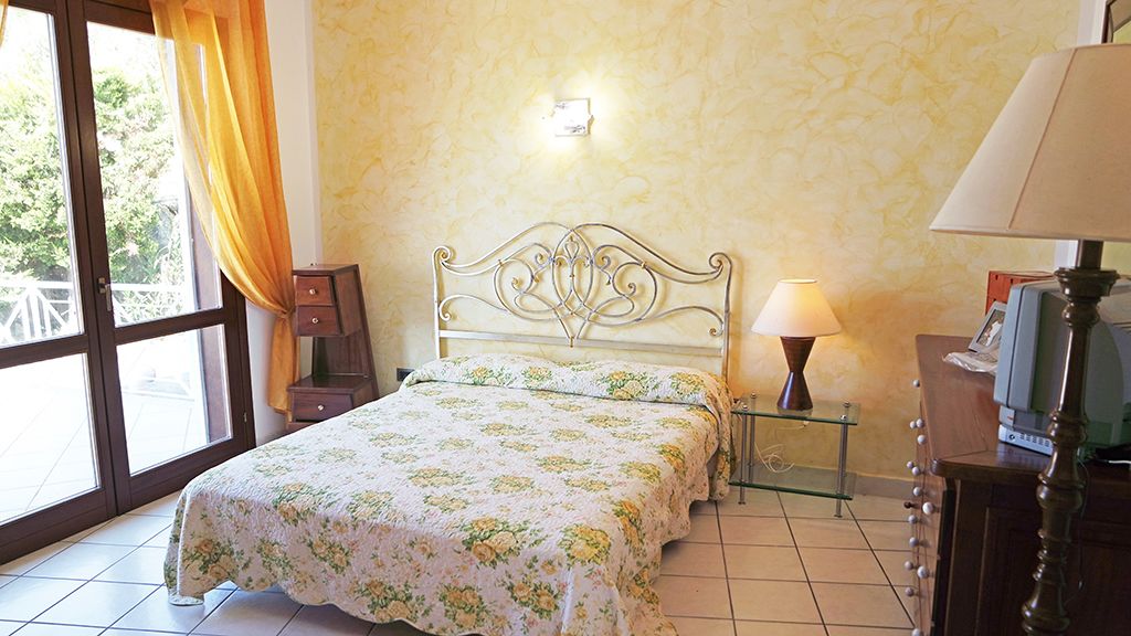 A bedroom with a bed, bedside lamps, a nightstand, and a window with curtains.