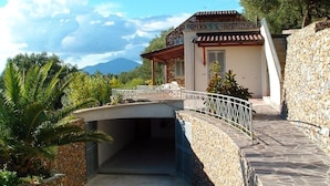 A house with a stone wall, a covered patio, and a view of mountains. - Villa Sarolli (Ascea)