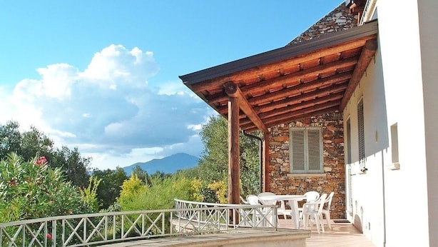 A covered outdoor area with a stone wall, white chairs, and a white railing. - Villa Sarolli (Ascea)