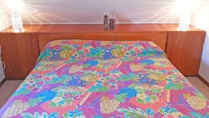 A bed with a colorful floral bedspread, wooden headboard, and two small glass containers on the headboard. - Villa Sarolli (Ascea)