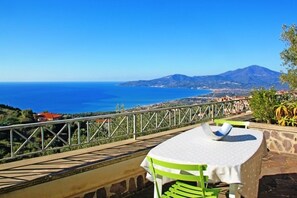 A terrace with a table and chairs overlooking a coastal view with a mountain in the distance. - Tempa delle Rose (Ascea)
