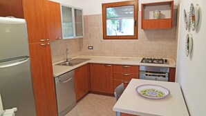 Een compacte keuken met houten kastjes, een roestvrijstalen koelkast, een ingebouwde oven en een kleine eettafel met een bord erop.