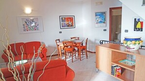 Een woonkamer met een rode bank, een eettafel met stoelen, en een houten kast vol boeken.