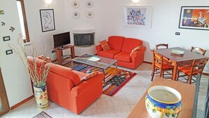 Een woonkamer met een bank, salontafel, televisie, open haard en een eethoek.