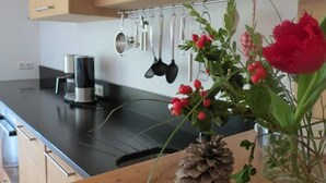 A kitchen with a coffee maker, hanging utensils, and a vase with flowers and a pine cone. - Mountainlodge Dorfhaus (Lenggries)