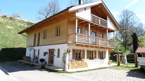 A two-story wooden house with a balcony, a stone wall, and a wooden fence. - Mountainlodge Dorfhaus (Lenggries)