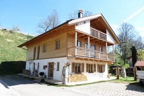 A two-story wooden house with a balcony, a stone wall, and a wooden fence. - Mountainlodge Dorfhaus (Lenggries)