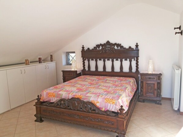 A bedroom with a wooden bed, a white wardrobe, a small bedside table, and a radiator.