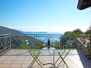 A terrace with a table and chairs, overlooking a scenic view of the sea and hills.