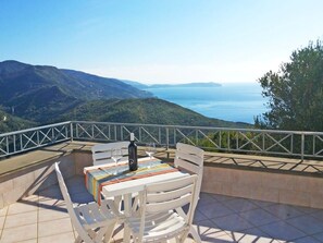 Una terrazza con tavolo e sedie, affacciata su un paesaggio montuoso e il mare.