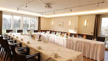A long dining table set for a formal event with multiple chairs, a projector, and a balcony view.