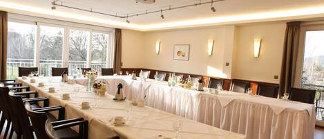 Una larga mesa de comedor dispuesta para un evento formal, con numerosas sillas, un proyector y vistas a un balcón.