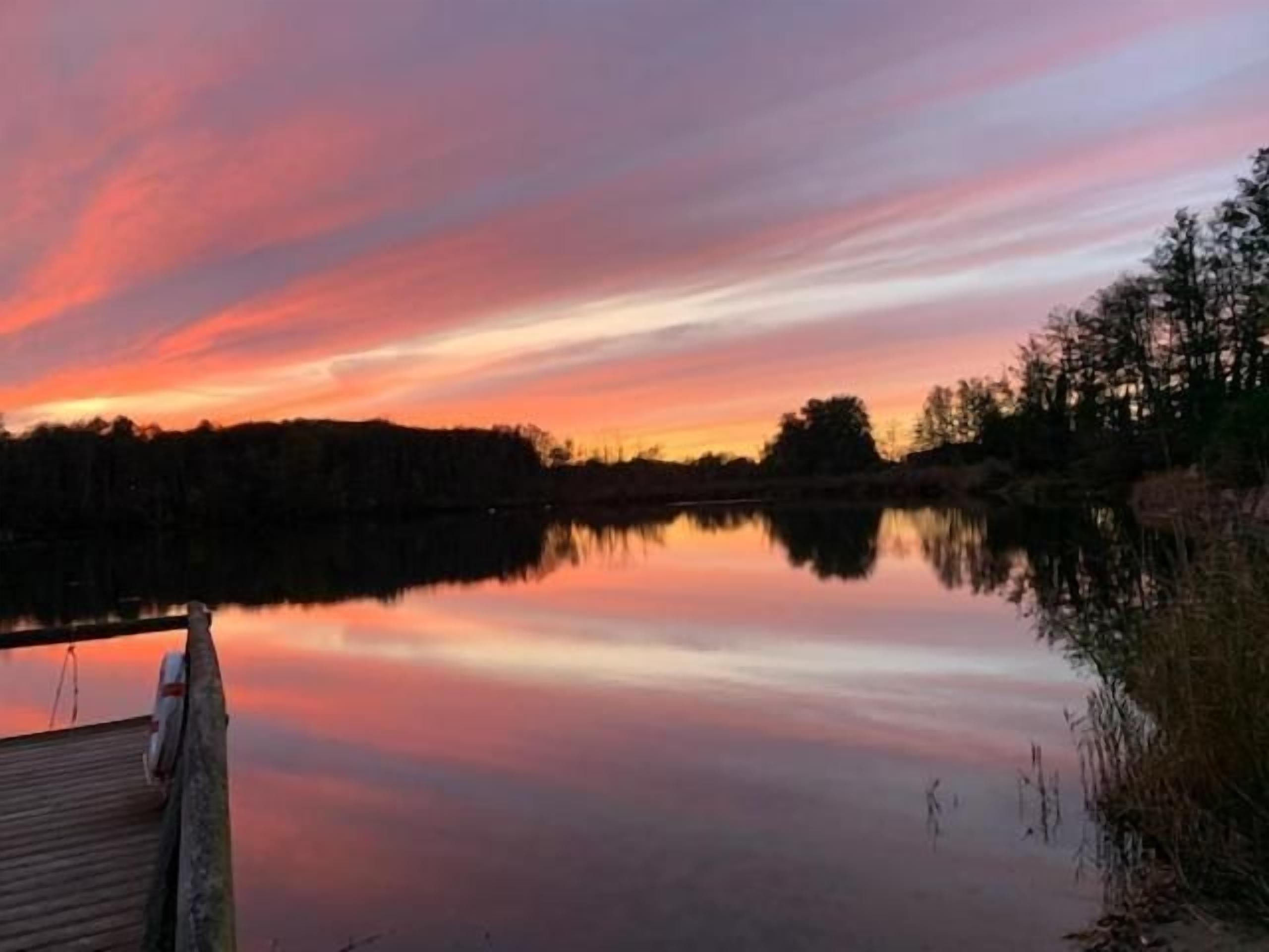 A calm lake at sunset with a dock extending into the water.