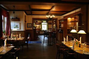 A restaurant with wooden interiors, multiple dining tables, and chandeliers. - Hotel Zum Rittmeister (Werder (Havel))