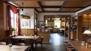 A restaurant with wooden tables and chairs, a central bar area, and a view of the dining area through a doorway. - Hotel Zum Rittmeister (Werder (Havel))