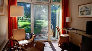 A room with a sliding glass door leading to a garden, wicker furniture, a desk with a computer, and a television. - Hotel Zum Rittmeister (Werder (Havel))