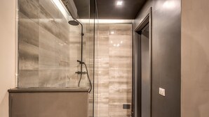 A modern bathroom with a glass-enclosed shower, tiled walls, and a dark door. - St. Eligio Suite (Rome)