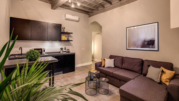 A modern living room with a brown sofa, two black side tables, and a large painting on the wall. - St. Eligio Suite (Rome)