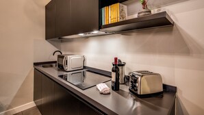 A modern kitchen with a built-in microwave, two toasters, a wine bottle, and a small plant on a shelf. - St. Eligio Suite (Rome)