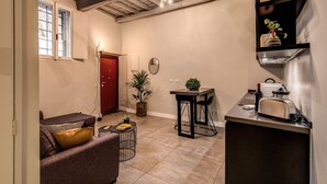 A compact living space with a kitchenette, a sofa, a dining table, and a red door. - St. Eligio Suite (Rome)
