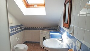 Un baño pequeño con tragaluz, lavadora y lavamanos.