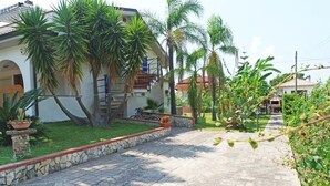 Propiedad residencial con entrada pavimentada, palmeras y pared de piedra.