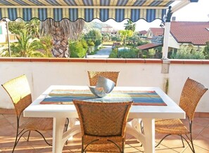Un espace repas comprenant une table et des chaises, donnant sur une rue résidentielle, et un patio couvert.