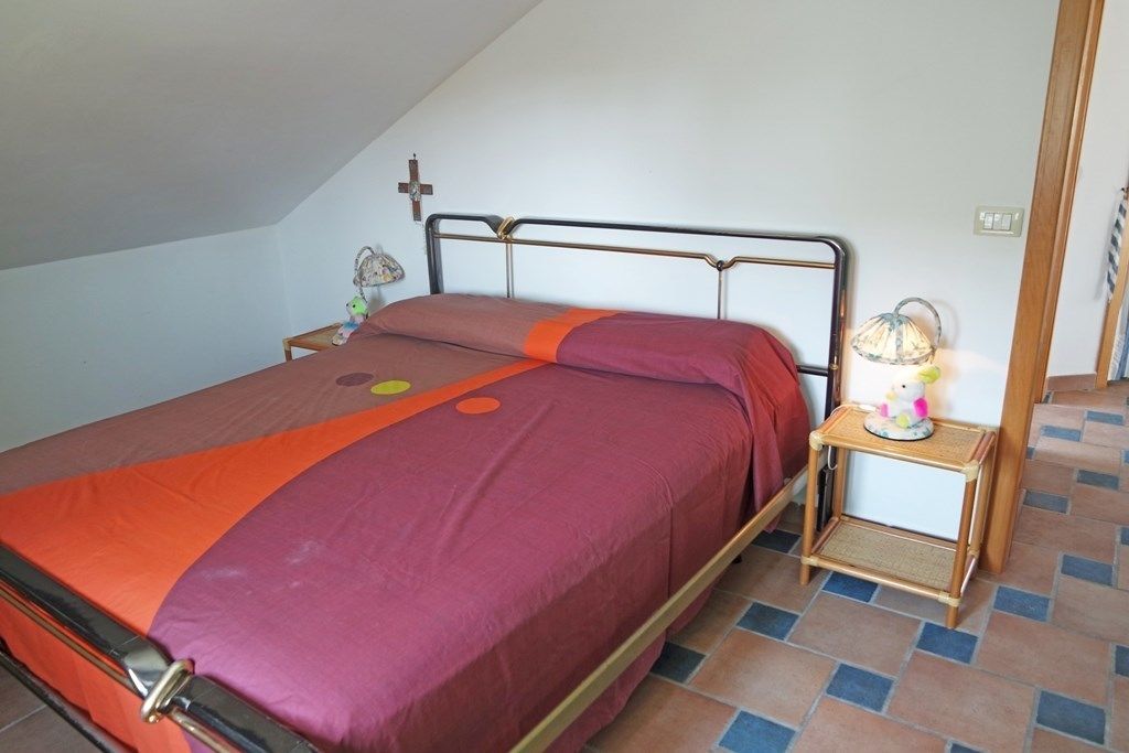 A single bed with a metal frame, a bedside table with a lamp, and a cross on the wall.