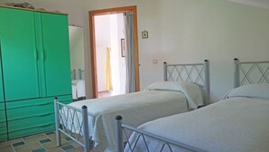 Una habitación con dos camas individuales, un armario verde y un baño visible a través de una puerta abierta.