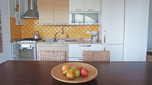 Eine Küche mit weißen Schränken, einer Edelstahl-Dunstabzugshaube, einer Mikrowelle und einem Spülbecken. Auf der Arbeitsfläche stehen Korbwannen und ein Holztisch mit einer Obstschale.