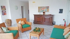 Ein Wohnzimmer mit Rattanmöbeln, einem grünen Sofa, einem Couchtisch mit Pflanze und einem Holzschrank.