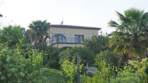 Ein zweistöckiges Haus mit Balkon, umgeben von üppiger Vegetation und Palmen.