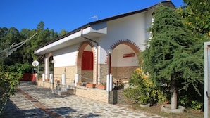 Un bâtiment dont l’entrée est pavée de pierres, avec des portes rouges et une façade blanche ornée de fenêtres en arc de cercle.
