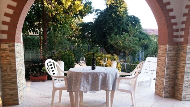 Une terrasse extérieure avec une table ronde et des chaises blanches, entourée d’une arche en briques.