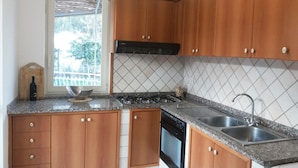 Une cuisine avec des meubles en bois, une cuisinière à gaz, un lave-vaisselle et une fenêtre donnant sur un espace verdoyant.