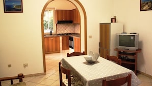 Une cuisine de taille réduite avec des meubles en bois, une table à manger recouverte d’une nappe à pois blancs et un téléviseur posé sur un meuble.