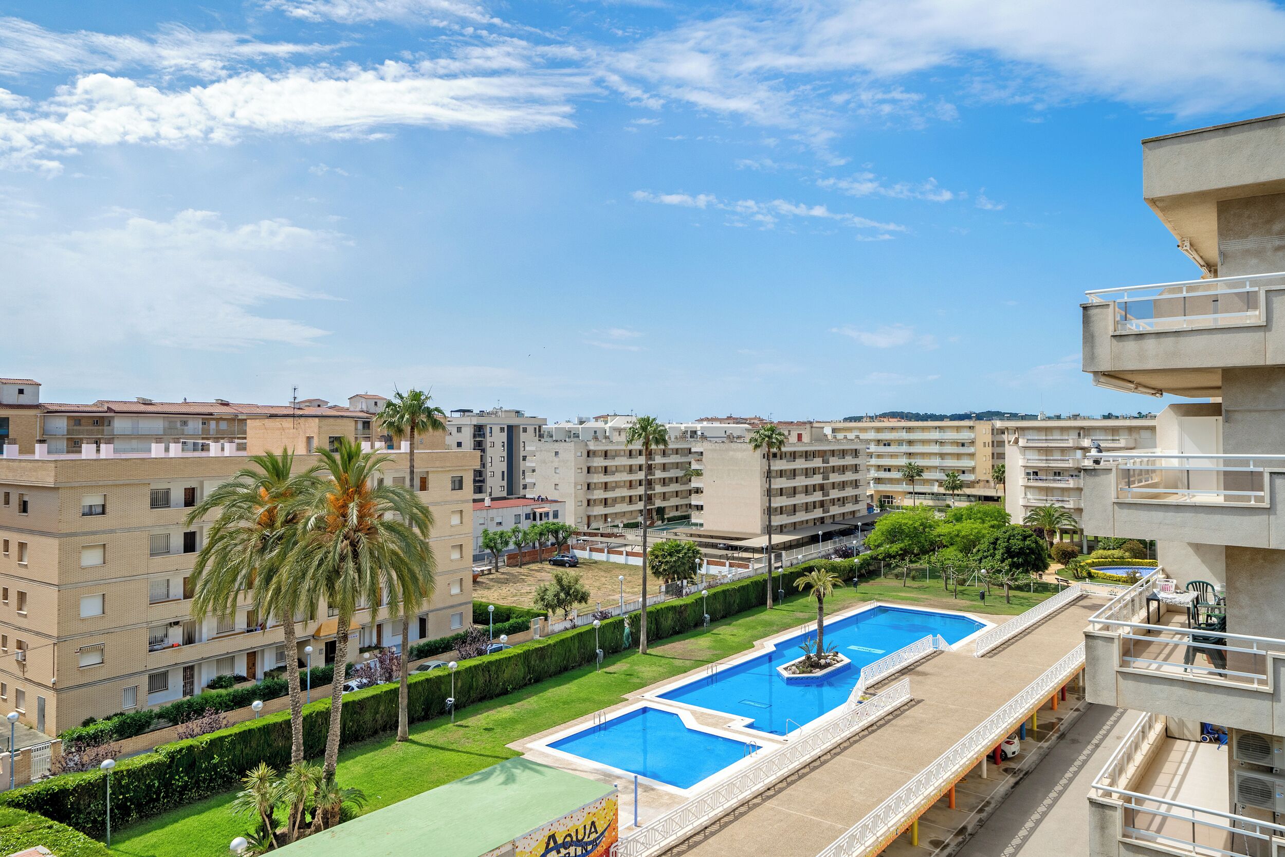 Un edificio residencial con piscina en la azotea, palmeras y cielo azul despejado.